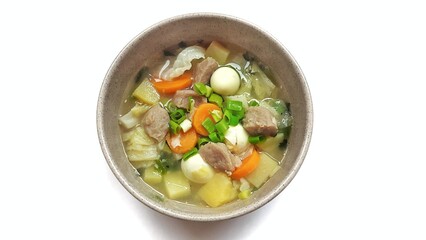 Sayur sop or vegetable soup, is an Indonesian food served on brown bowl. Isolated on white background. Food presentation photography