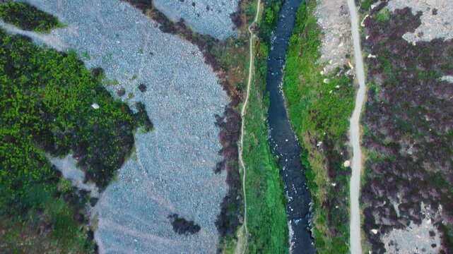 Top Down Forward Moving Aerial View of Wninding River with Scattered Rocks on Hillside with Hiking Path. Aerial View of British Countryside.