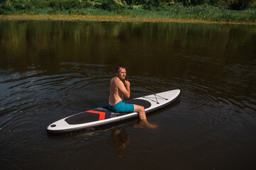 Man rides on a SUP board on the river in the middle of the forest, summer active outdoor recreation 
