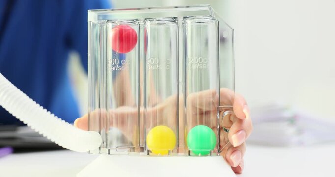 Woman holds respiratory spirometer featuring chambers with colored balls rising inside. Concept of lung function assessment and breathing exercises