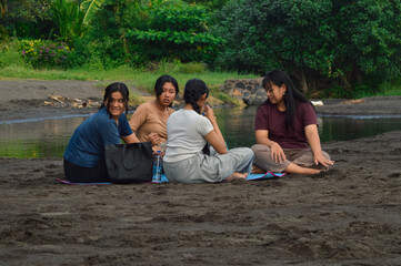 Four teenage girls enjoy a peaceful morning sitting together on a beach mat near a brackish water...