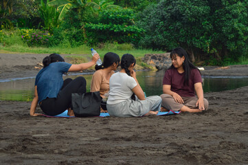 While three girls remain seated on a beach mat, one teenage girl begins to stand up as if preparing...