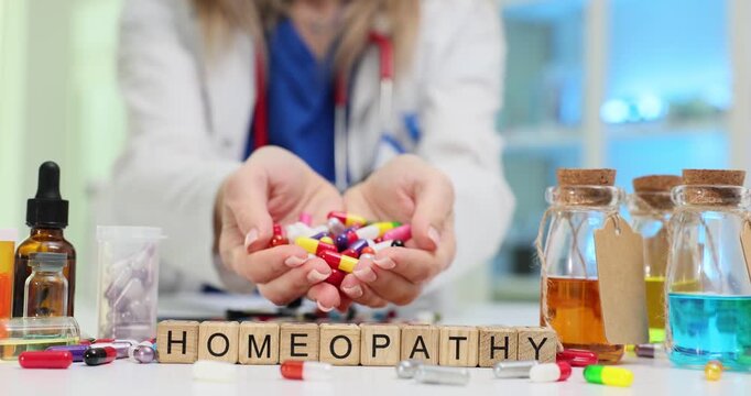 Woman holds out handful of colorful capsules near Homeopathy on blocks and bottles by scattered pills. Alternative medicine and associated remedies