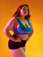 Self-assured woman posing against lively orange background. Concept of vivid body expression, radiant energy in fashion campaigns, confident sportswear identity.