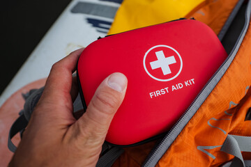 A person is firmly holding a bright red first aid kit tightly in their hand, always prepared for...