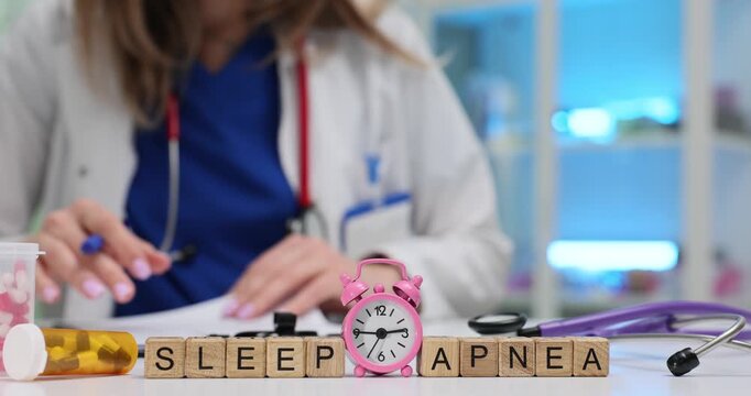 Doctor reviews documents at desk with Sleep Apnea on blocks and alarm clock. Sleep disorder awareness and importance of timely medical attention