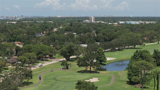 Aerial view of Florida golf course, lush fairways, nearby homes, scenic pond, coastal skyline, and blue skies&mdash;perfect blend of leisure, nature, and suburban lifestyle.