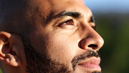 Close-up profile of a contemplative man gazing upward, sunlit skin, and short beard