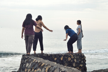 A group of girls stands playfully near the sea, with waves lapping at the beach as they enjoy the morning together.