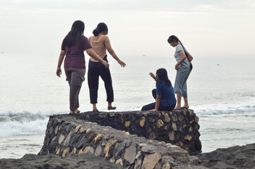 One girl sits calmly admiring the ocean view, while the others engage in fun conversation nearby by the foamy edge of the beach.