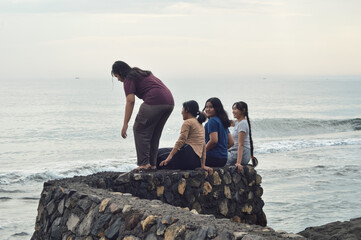 Four teen girls gather on the rocky ledge, chatting and enjoying the tranquil ocean waves that roll gently onto the shore.