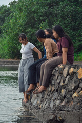 A girl climbs back up from the stream toward her friends who are still sitting on the sandy beach, surrounded by natural beauty.