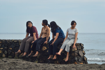 A group of teen girls enjoys casual conversation and quiet bonding as they sit close together near the ocean during a calm morning.