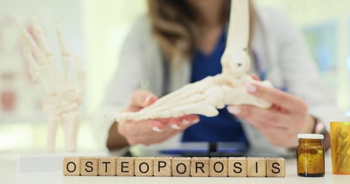 Medical professional holds foot bone model near Osteoporosis on wooden blocks on desk. Focus on educational and diagnostic aspects of osteoporosis