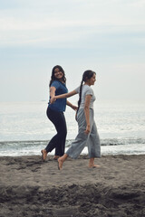 While walking along the beach hand in hand, one girl glances back playfully, as both continue enjoying their joyful morning stroll near the waves.