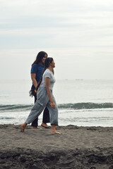 With calm smiles, the girls stroll across the damp beach sand, waves lapping nearby, their hands clasped tightly as they enjoy the morning together.