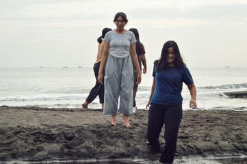 On a tranquil beach morning, a girl heads to the shallow water as her friends explore the coastline and enjoy the natural scenery.
