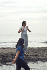 Two teen girls enjoy the morning beach as one walks into the shallow brackish water, smiling while the other watches nearby.