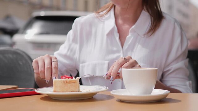A woman savors a slice of cake and sips coffee at an outdoor cafe in the city. The midday atmosphere is vibrant as she enjoys her treat.