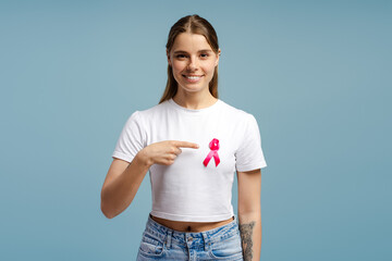 Young woman pointing at pink ribbon for breast cancer awareness, prevention and fundraising campaign