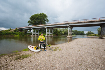 An adventurous individual is meticulously preparing for an exciting paddleboard journey beneath a...