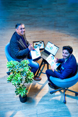 Indian corporate partners collaborate while seated at desk using laptop in top-angle office view
