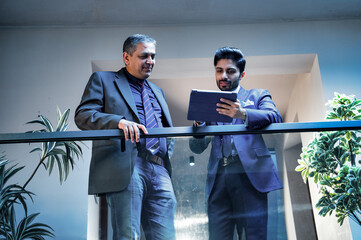 Two Indian executives sharing ideas using tablet near glass partition in modern corporate office