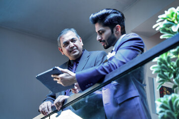 Two Indian executives sharing ideas using tablet near glass partition in modern corporate office