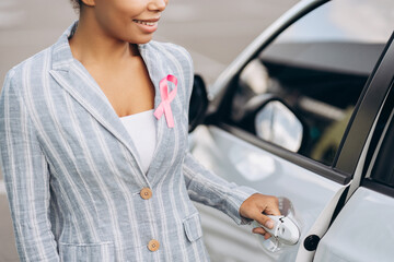 Close up of young woman with pink ribbon supporting breast cancer awareness opening car door