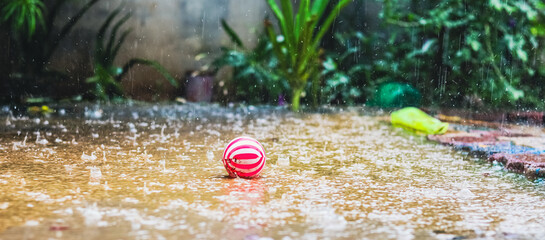 A red and white striped ball lying on a rain-soaked ground during a heavy downpour in a garden...