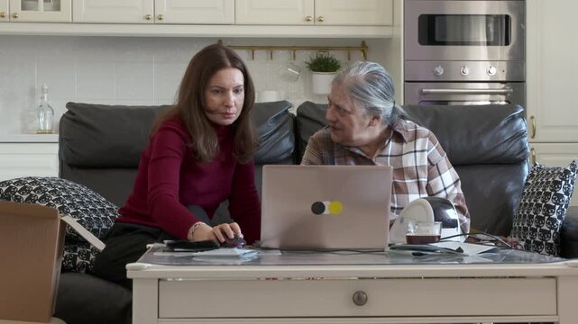 A woman is patiently teaching her elderly mother how to use a laptop and thermal label printer for her online store's trading activities, in a comfortable home setting.