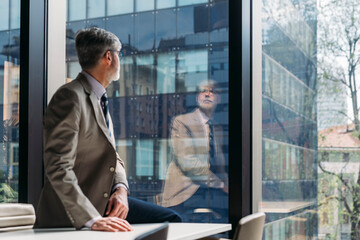 Businessman sitting on desk looking through window in office