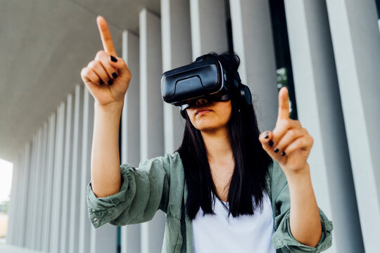 Young woman wearing virtual reality simulator pointing in front of column