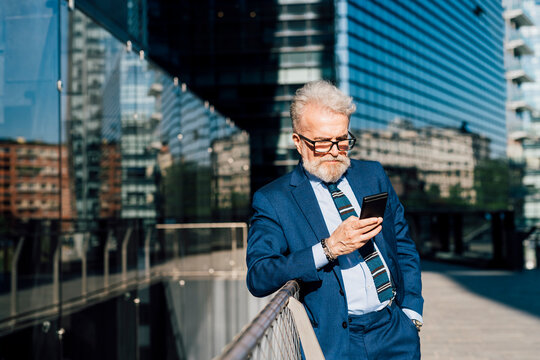 Senior businessman working on smart phone standing outside office building