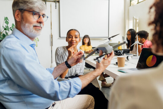 Businessman with quadcopter sitting by colleagues in office at workplace