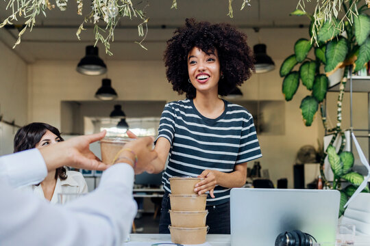 Happy businesswoman passing lunch box to colleague at office