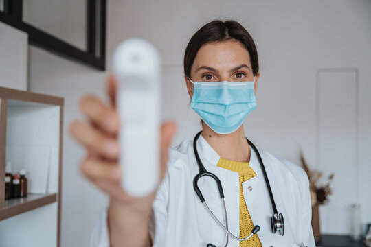 Doctor with protective face mask holding thermometer in clinic