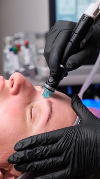 Young woman gets skincare treatment with a professional rejuvenation device. Facial therapy session in a beauty salon. Vertical video