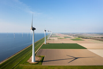 Wind turbines near sea on sunny day at field