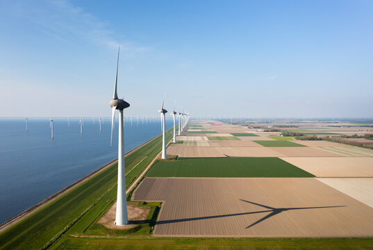 Wind turbines near sea on sunny day at field