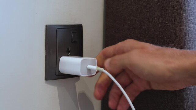 Hand inserting a white charging adapter into a wall socket. Close-up view inside a modern interior.