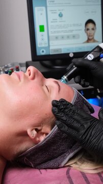 Facial therapy session in a beauty salon. Young woman gets skincare treatment with a professional rejuvenation device.