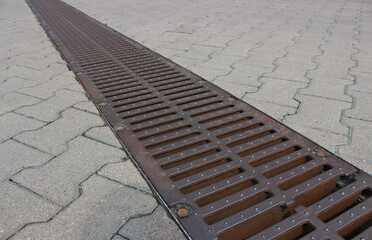 A strong storm drain grate on the surface of evenly laid outdoor tiles 
