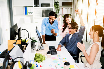 Diverse business team celebrating success in modern office. Group cheers joyfully at computer screen, showing teamwork, achievement, and motivation in a productive, collaborative workspace.
