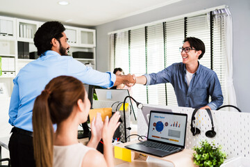Diverse team celebrating success in a modern office. Two male colleagues shaking hands while a female coworker applauds. Smiling, teamwork, achievement, and collaboration in business setting.