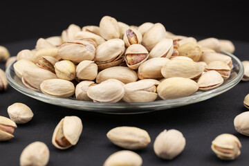 Heap of tasty pistachio nuts on the plate on dark background