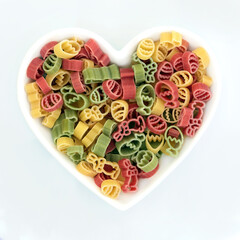 Heart shape dish of tricolor dried pasta with easter theme symbols of eggs, bunny rabbits, tulip flowers in red green, yellow colors. Fun romantic carbohydrate food on white.