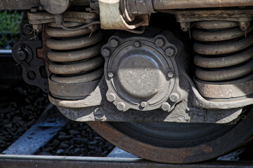 Close-up of modern railcar wheelset showcasing robust coil springs, brake assembly, and steel components on track ballast under natural daylight. Photo