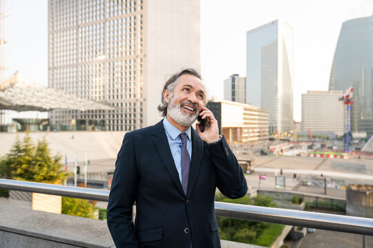 Happy mature businessman talking on smart phone standing by railing