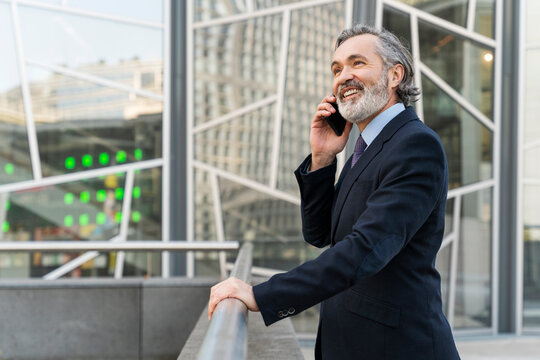 Happy businessman talking on smart phone standing by railing